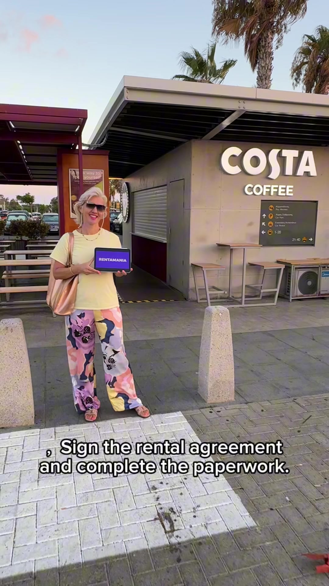 Представитель Rentamania с табличкой возле Costa Coffee в аэропорту Пафоса
